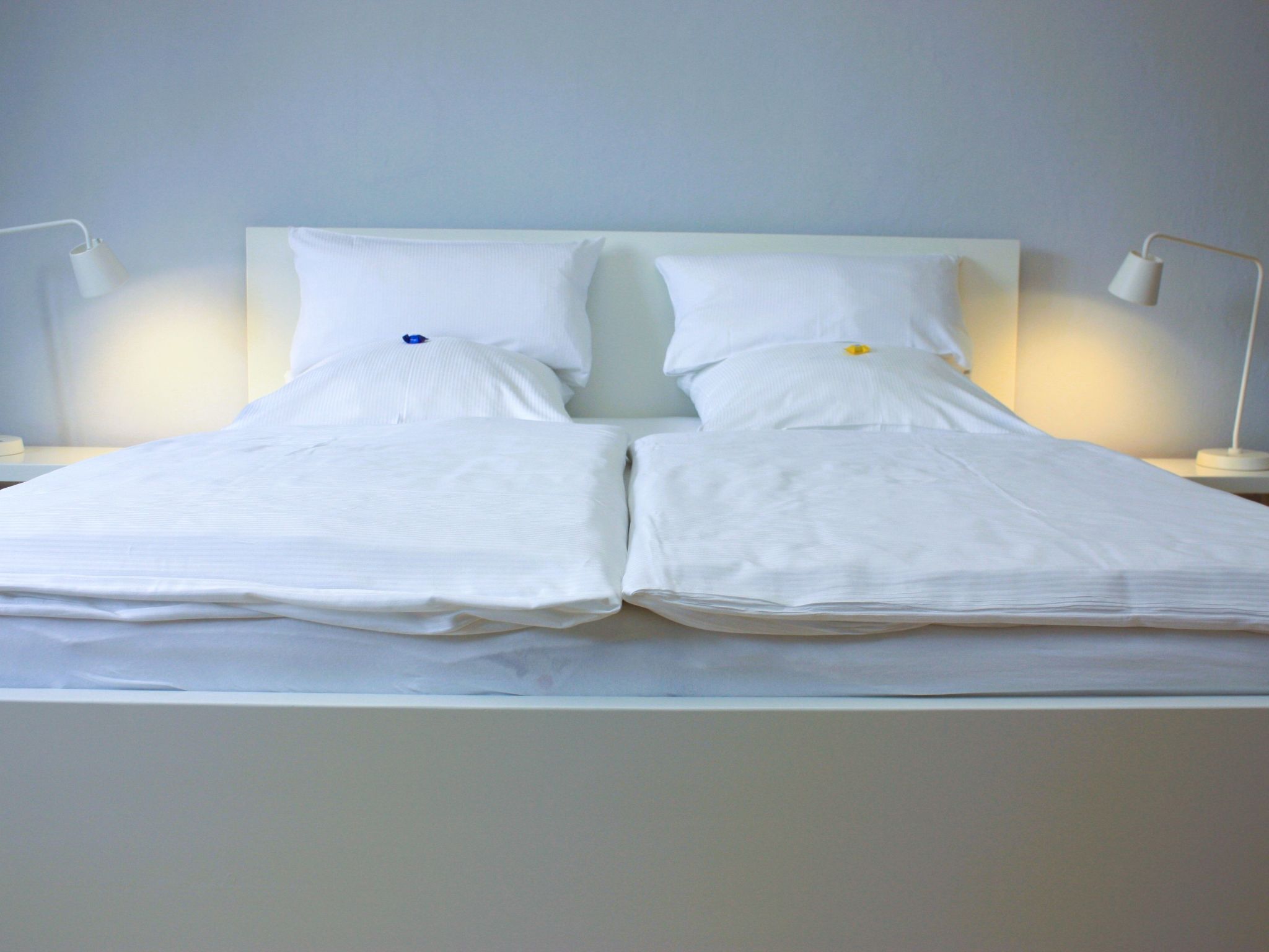 Un lit double bien fait, avec du linge de lit blanc et des oreillers, et de chaque côté, une lampe de chevet.