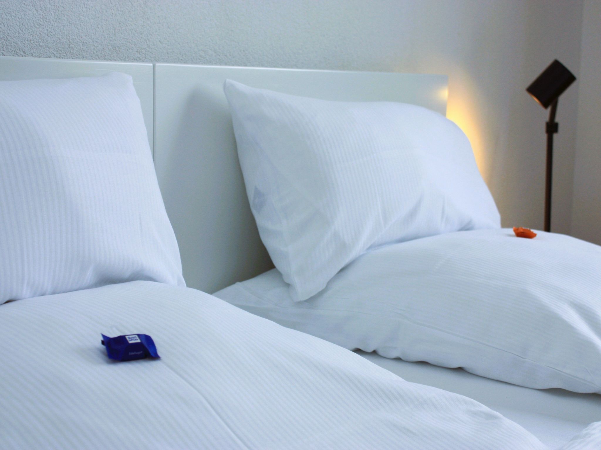 Ein Hotelzimmer mit zwei Betten, weißer Bettwäsche und einem Nachttisch mit Lampe.