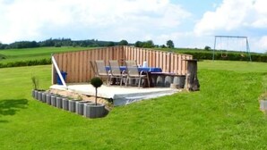 Une structure en bois dotée d’un patio, de sièges extérieurs et d’une balançoire installée dans un champ herbeux.