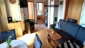 Un salon confortable avec un canapé, une petite table et un téléviseur. Il y a également un coin cuisine avec une cuisinière et une table à manger avec des chaises.