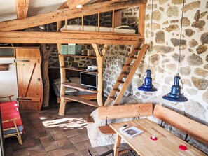Una habitación rústica con cama en literas, estantes de madera, un escritorio y paredes de piedra.