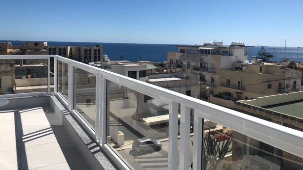 A high-rise building with a glass balcony overlooking a cityscape and the sea. - 3. Appartement mit Meerblick in Strandnähe by Interhome (Marsascala)