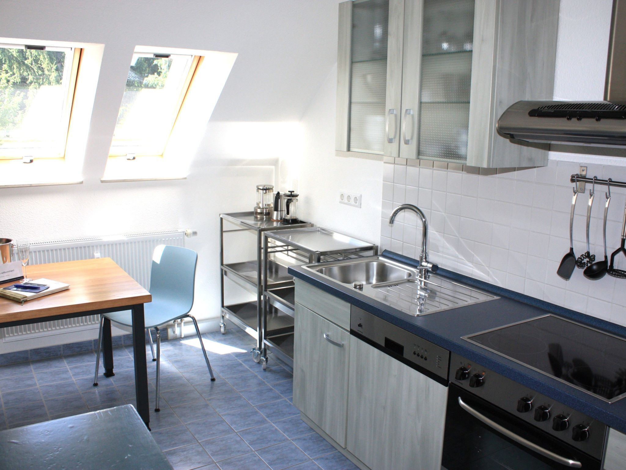 A modern kitchen with a built-in dishwasher, a stove, and a sink. There is a dining table with chairs and a window providing natural light.