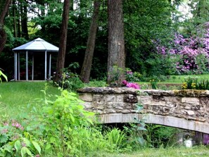 A stone bridge over a small stream in a lush garden with a gazebo in the background. - Wohlfühloase für Natur- und Gartenliebhaber by Interhome (Walkenried)