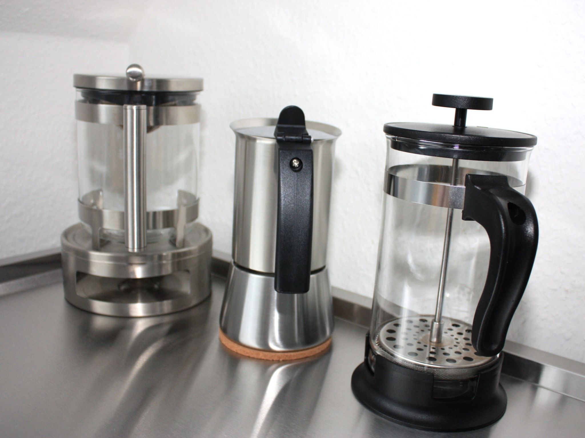 Tres cafeteras sobre una encimera de acero inoxidable.