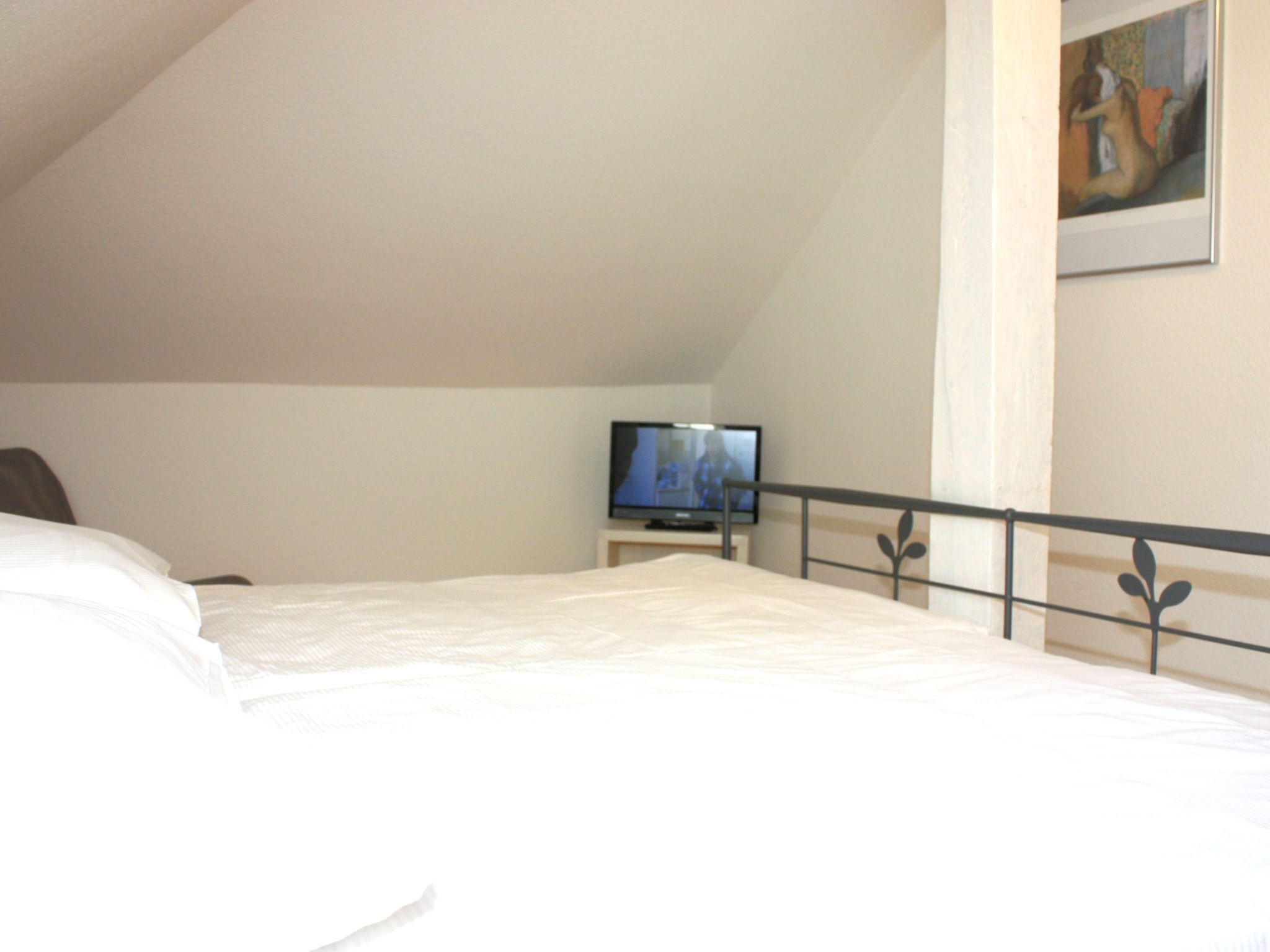 A bedroom with a bed, a television on a nightstand, and a painting on the wall.