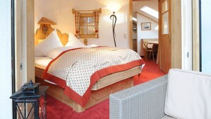 Ein gemütliches Schlafzimmer mit Holzbalkendecke, einem Bett mit gemustertem Überwurf, einem Nachttisch mit Laterne und Korbmöbeln.