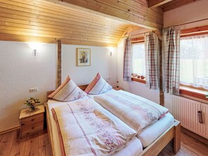 Une chambre à coucher dans une cabane en bois, avec un lit, des oreillers, une table de chevet, un tableau au mur et une fenêtre avec des rideaux.