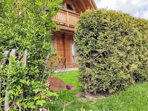 Eine Holzhütte mit einem Balkon, umgeben von üppigem Grün und einem kleinen Garten.