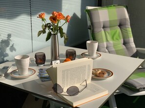 Ein Tisch mit einem Buch, Brillen, einer Tasse, einem Teller mit Keksen, einer Vase mit Blumen und einem Smartphone.