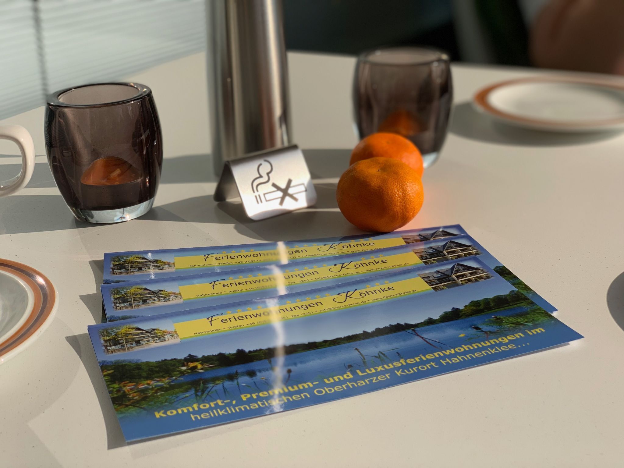 Une table avec une brochure, deux verres, une orange et un récipient en métal.