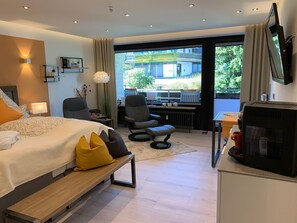 Ett modernt hotellrum med en stor säng, ett skrivbord med en stol, en TV och utsikt över omgivningarna.