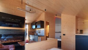 A modern, compact room with a wooden interior, a bed, a small seating area, and a kitchen with a built-in stove.