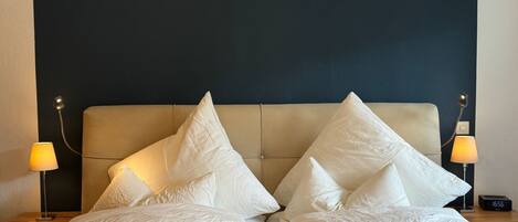 A neatly made bed with white linens and pillows, two bedside lamps, and a digital clock on a bedside table.