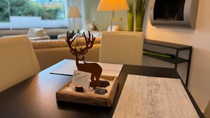 Un soggiorno moderno con un tavolo di legno su cui sono esposti un cervo decorativo, un cartello di benvenuto e un foglio di carta. Si notano anche un divano, una lampada e un televisore sullo sfondo.
