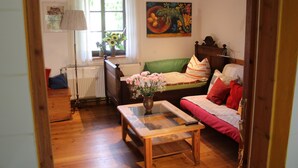A cozy room with a wooden floor, a green sofa with red cushions, a wooden coffee table with a vase of flowers, and a painting on the wall. - Daddeldu by Interhome (Börgerende)