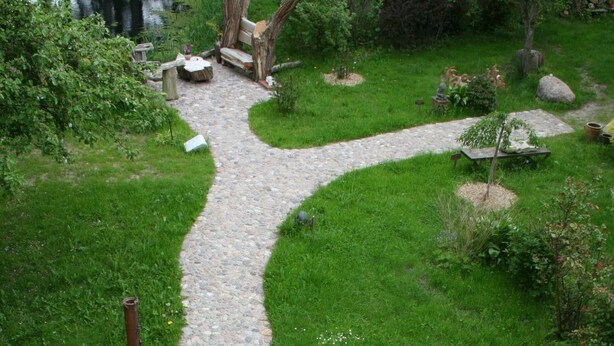 A garden with a winding stone path, various plants, and rustic wooden furniture. - Daddeldu by Interhome (Börgerende)