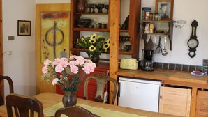 En matplats med ett träbord, stolar, en vas med blommor, en kaffemaskin och ett kylskåp.