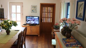 Ett mysigt vardagsrum med ett matbord i trä, en tv, en bokhylla och en vas med blommor.