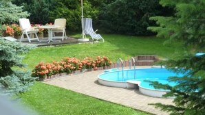 Een achtertuin met een zwembad, een terras met stoelen en een gele parasol.