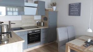 A modern kitchen with grey cabinets, a built-in oven, a coffee maker, and a dining area with a table and chairs. - in Strandnähe by Interhome (Bad Doberan)