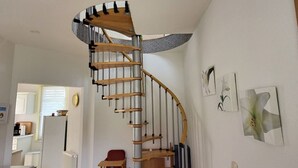 Una escalera de caracol con escalones de madera y barandillas de metal en un área moderna de cocina y sala de estar.