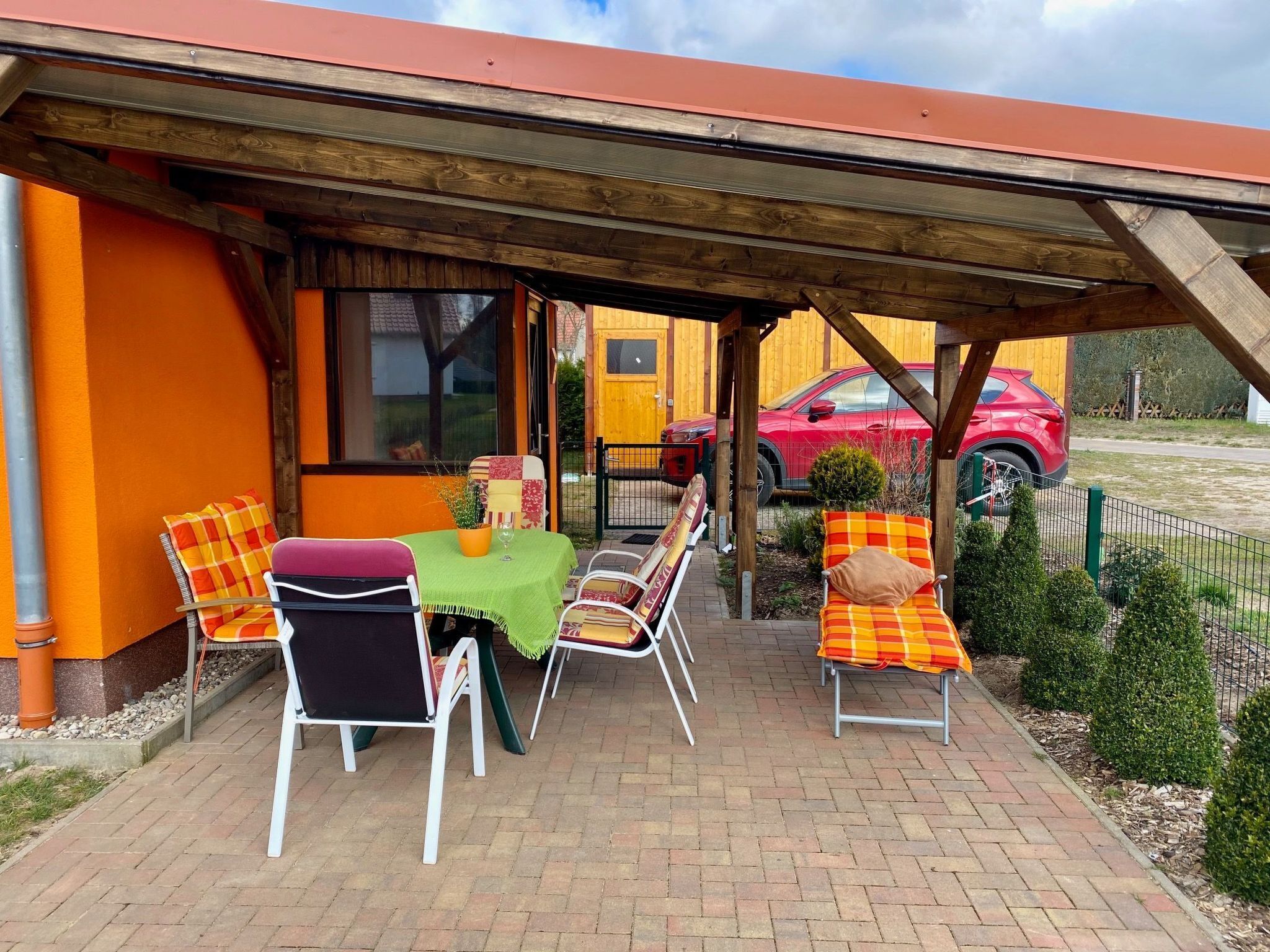 Un patio esterno con tavolo e sedie, un'area salotto coperta e un'auto parcheggiata sullo sfondo.