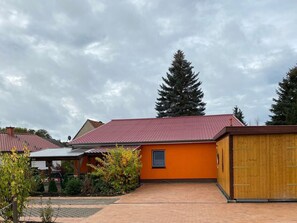 Ein Wohngebäude mit rotem Ziegeldach, einer orangefarbenen Außenwand und einer Holztür zur Garage.