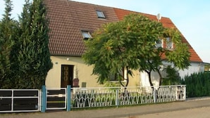 Een huis met pannendak, een voordeur en een omheinde tuin.