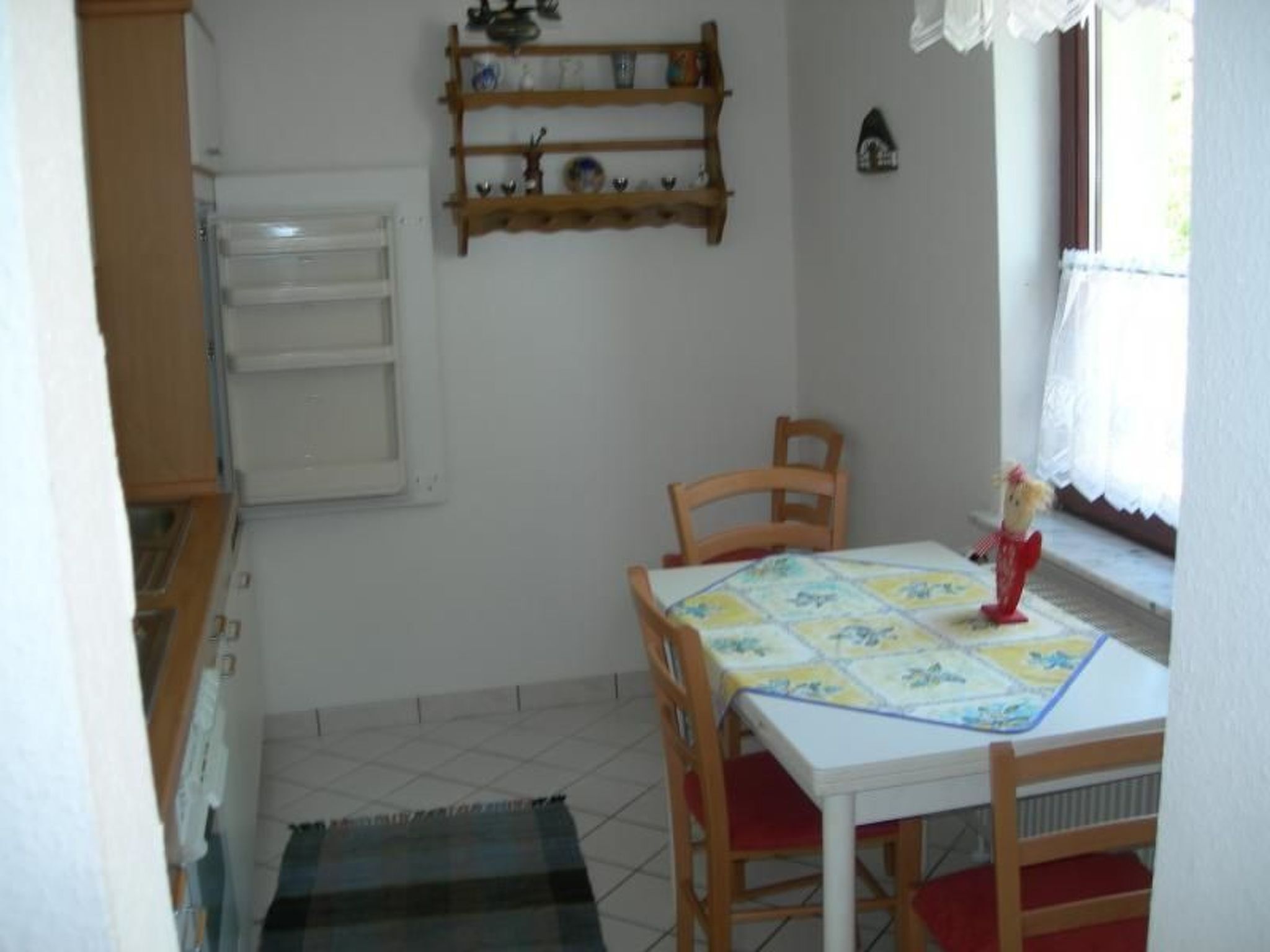 Een gezellig eetgedeelte met een tafel, stoelen, een plank met servies en een raam met gordijnen.