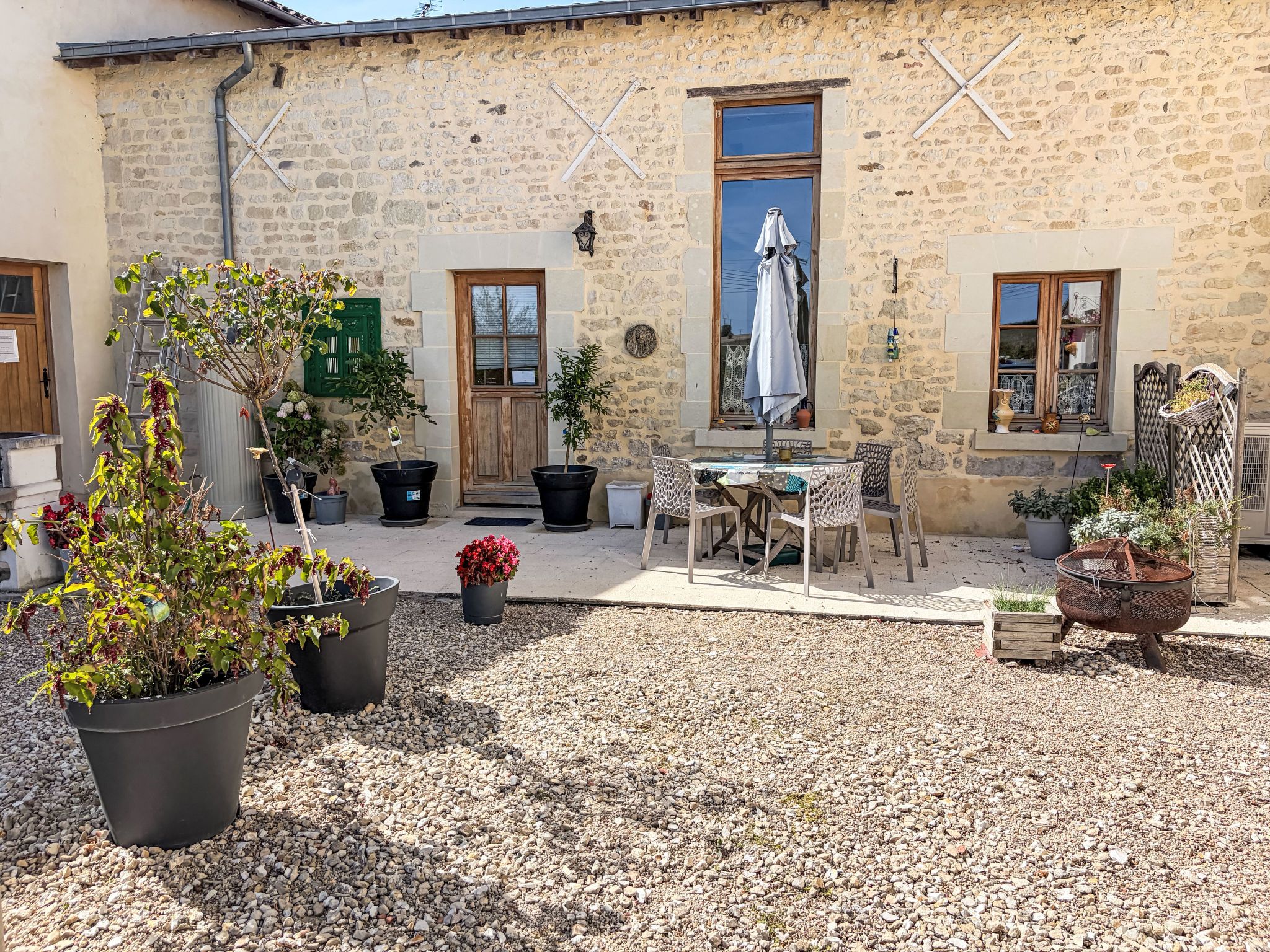 Un patio con mobiliario exterior, macetas con plantas y un edificio de piedra con puertas y ventanas de madera.