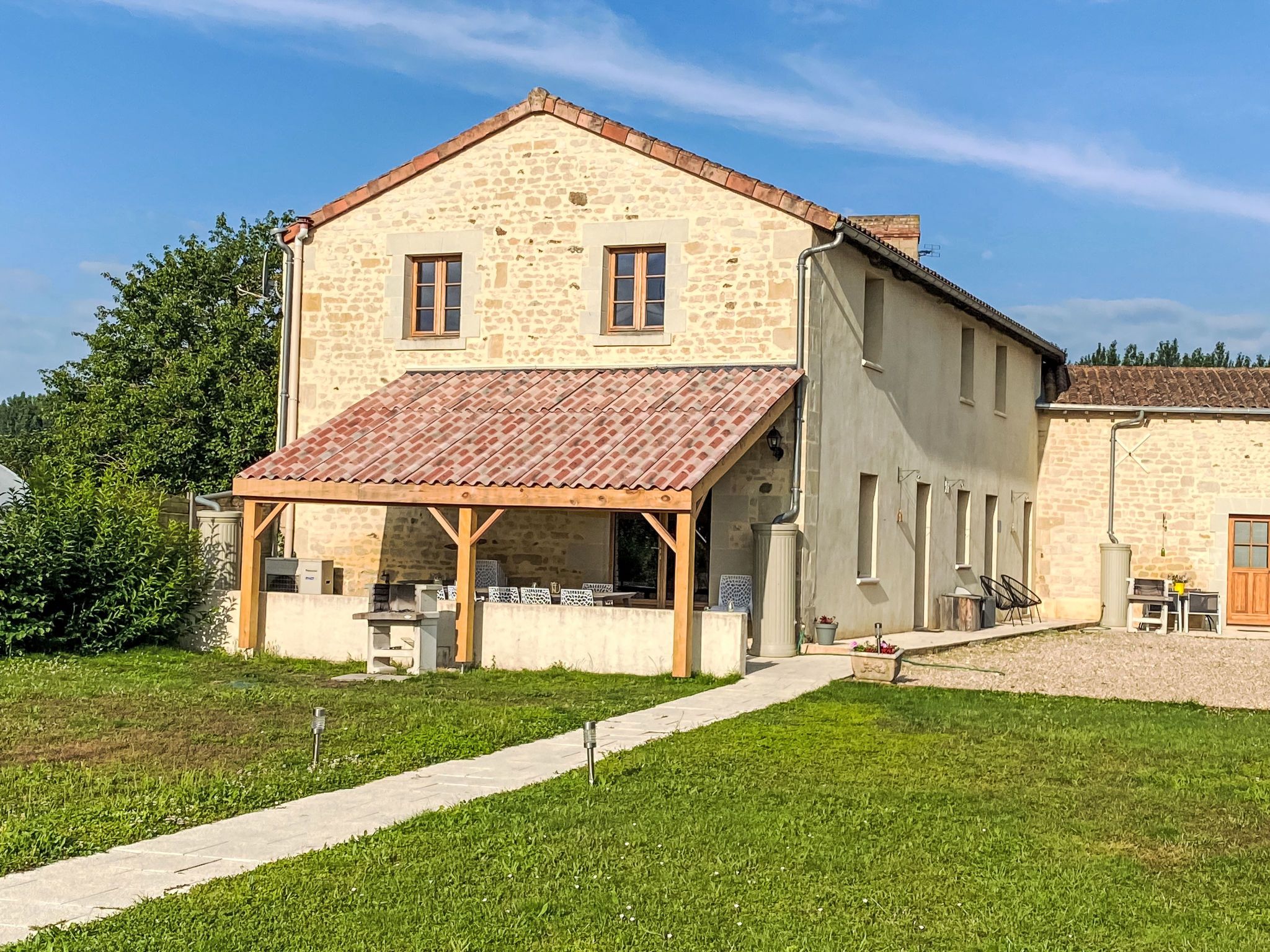 Un bâtiment en pierre avec un toit en tuiles, un patio couvert et un chemin pavé.