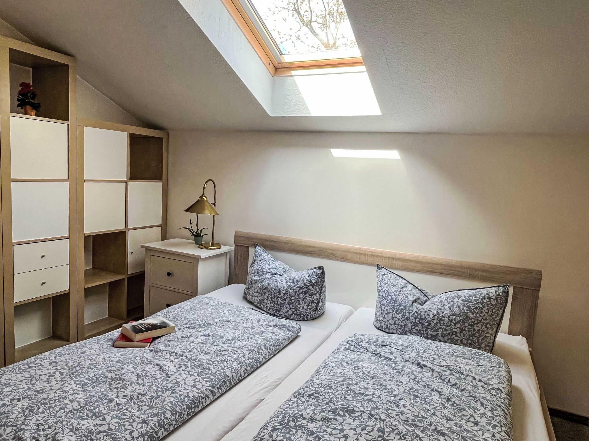 Une chambre avec un puits de lumière, une table de chevet avec une lampe et un lit avec une literie à motifs floraux.