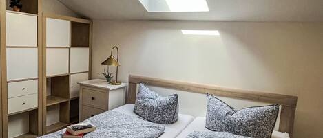Une chambre avec un puits de lumière, une table de chevet avec une lampe et un lit avec une literie à motifs floraux.