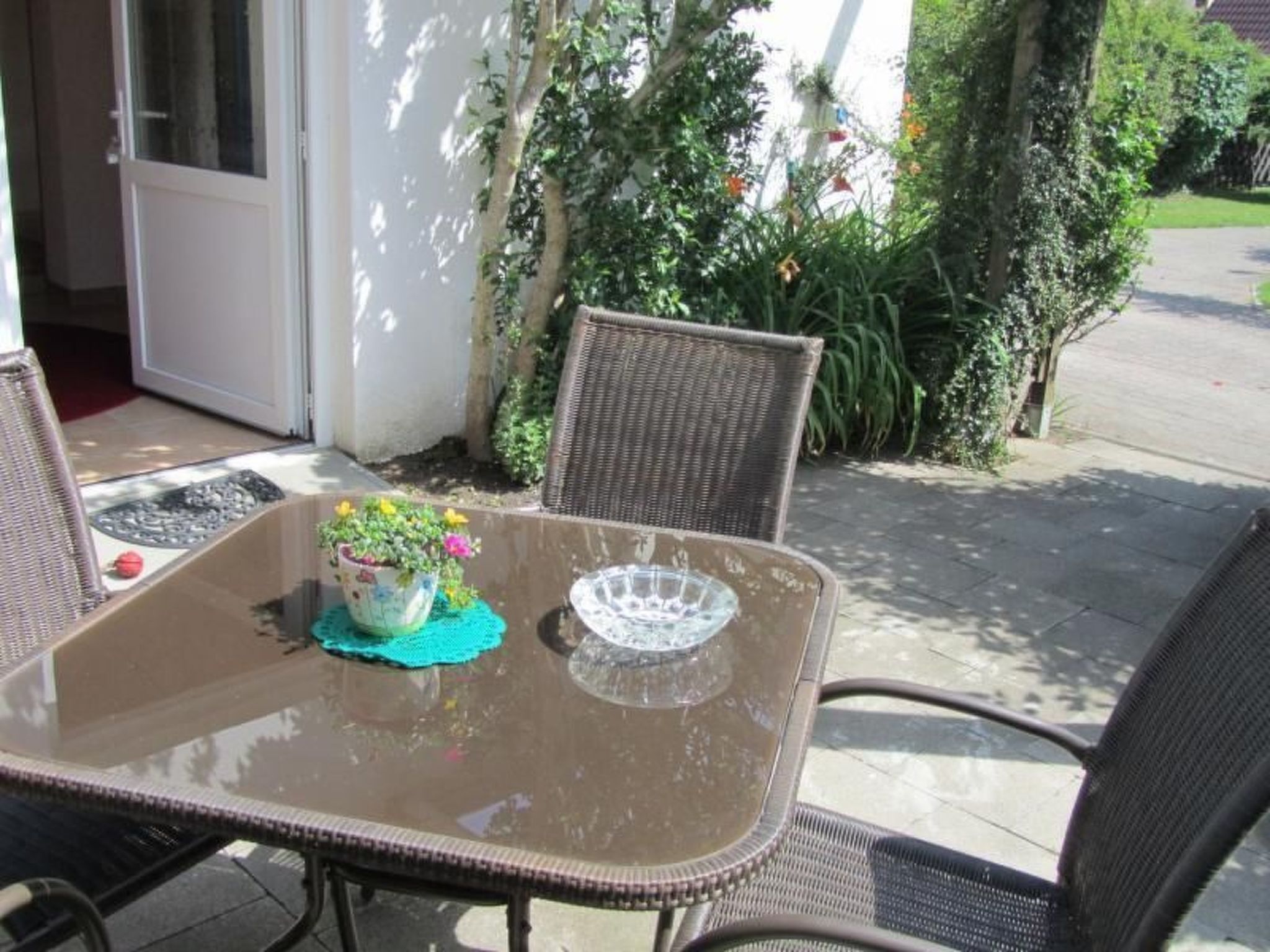Eine Terrassengruppe im Freien mit einem Tisch aus Glasplatte, Korbstühlen und einem Blumentopf.