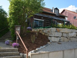 Un bâtiment doté d’un mur de soutènement en pierre, d’une clôture en métal et d’un escalier menant à une porte.