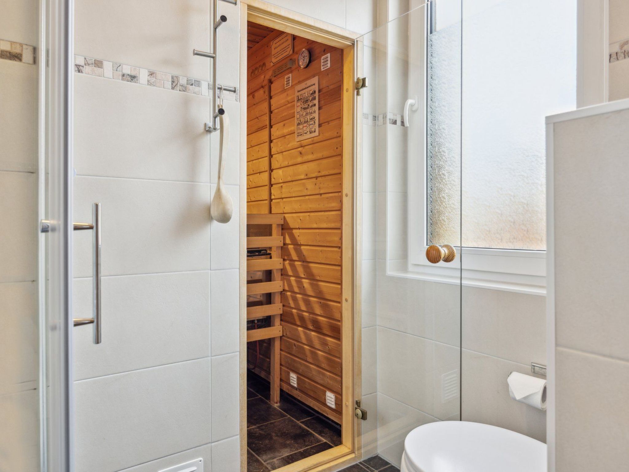 Et badeværelse med en trædør til sauna, toilet og bruseområde.