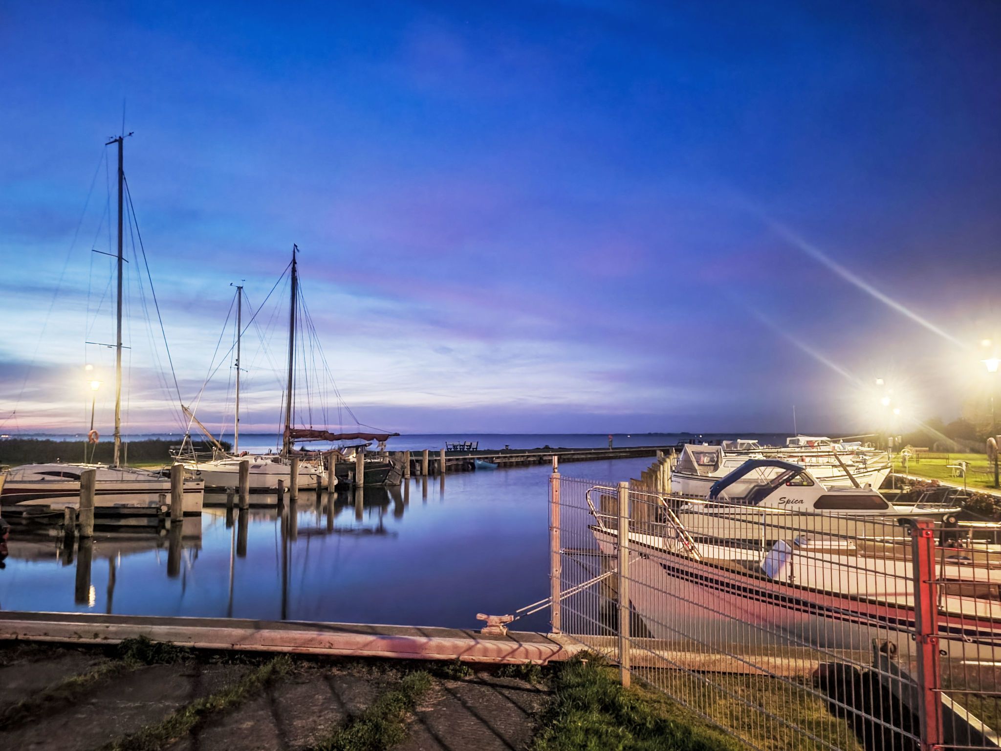 A marina with boats docked, a calm water surface, and a clear sky.