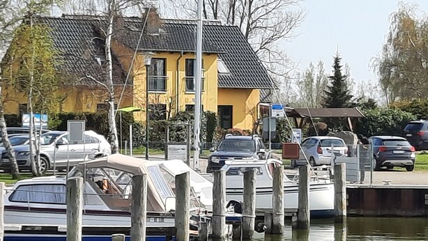 Uma marina com barcos atracados, um edifício amarelo e carros estacionados.
