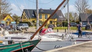 Uma marina com vários barcos atracados, um cais de madeira e casas ao fundo.