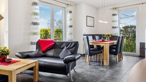 Uma sala de estar moderna com um sofá de couro preto, uma mesa de centro de madeira e um espaço de jantar com mesa e cadeiras de madeira.