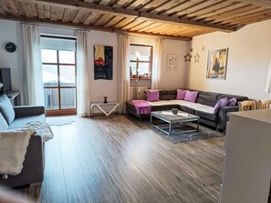 A living room with a sofa, coffee table, and a TV. There are windows with curtains, a clock, and artwork on the walls. - Waldesruhe 303 by Interhome (Hauzenberg)