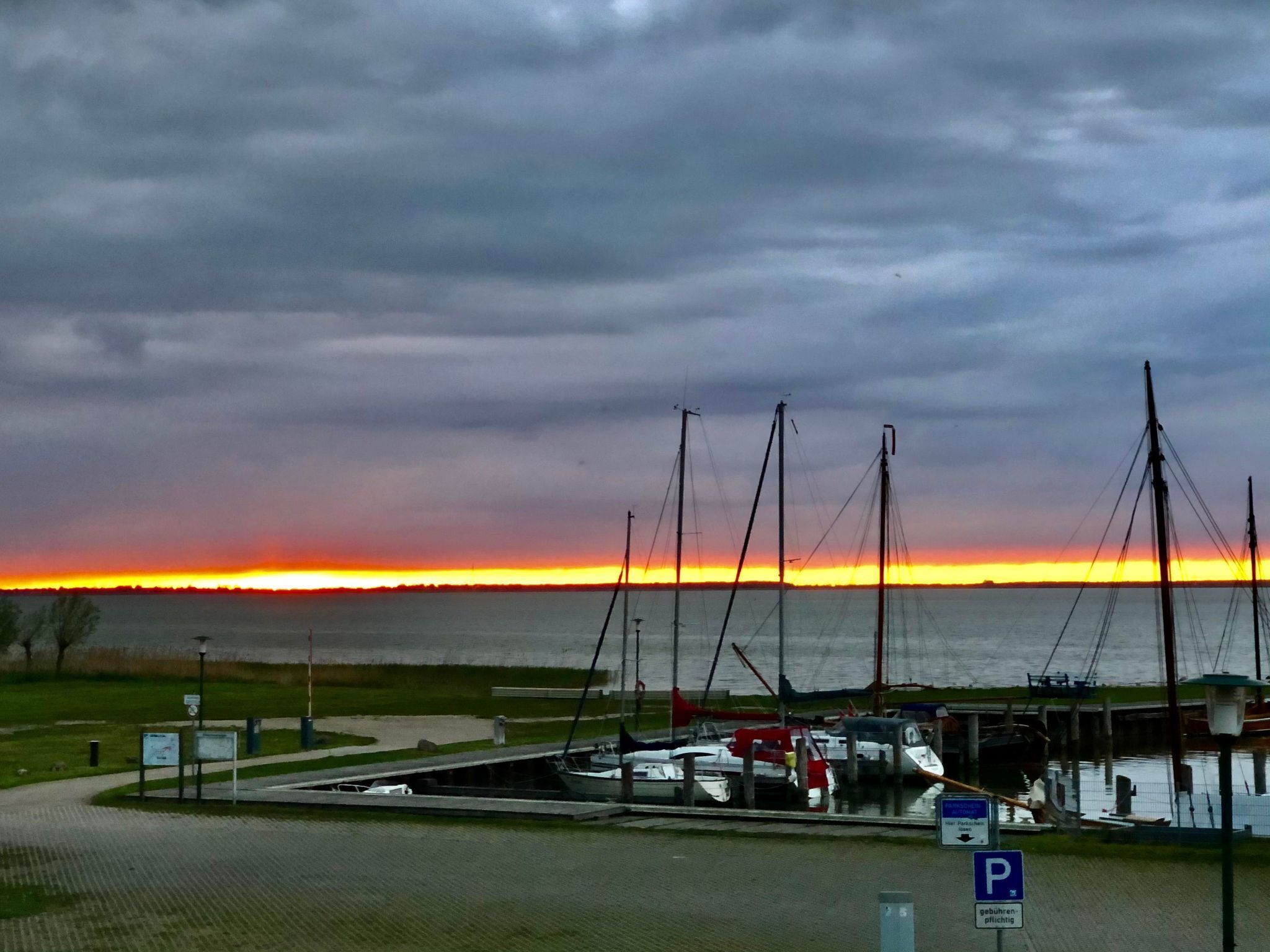 Un puerto deportivo con barcos amarrados, un cartel de estacionamiento y un atardecer sobre el agua.