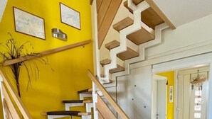 Una escalera con peldaños de madera y barandilla blanca, que conduce a una habitación con paredes amarillas y una puerta.