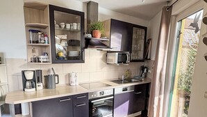 Una cocina moderna con horno empotrado, microondas y fregadero. Se aprecia una ventana con vista a follaje exterior.