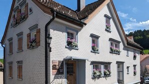 Perinteinen, eurooppalaistyylinen rakennus, jossa on useita ikkunoita ja ikkunalaatikkoja, joissa kasvaa kukkia.
