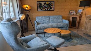 Moderni olohuone, jossa on harmaa nojatuoli, kuviollinen sohva ja kaksi pyöreää puista sohvapöytää.