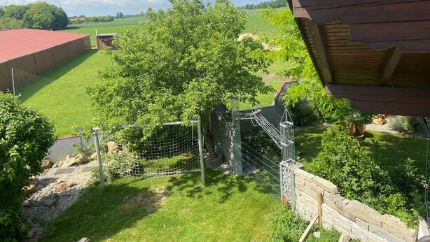 A view of a fenced outdoor area with a tree, a stone wall, and a building with a red roof. - Appartement Wimmer by Interhome (Bad Füssing)
