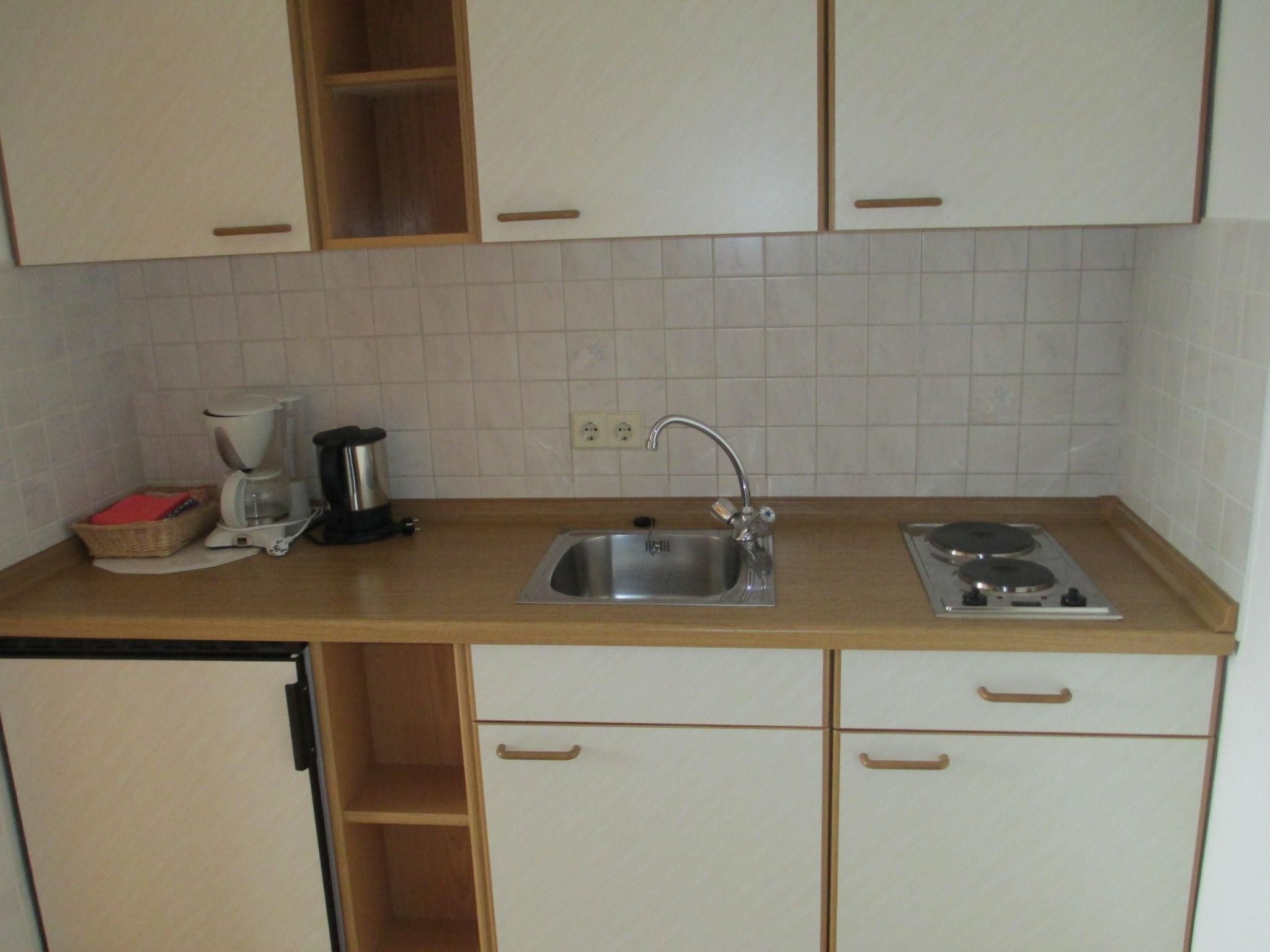 Cocina compacta con lavamanos, estufa y cafetera.