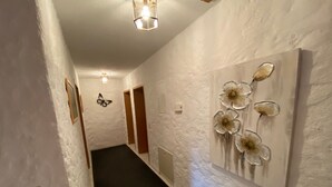 A hallway with white textured walls, a black carpet, a butterfly wall decoration, and a flower wall art piece. - Appartement Wimmer by Interhome (Bad Füssing)